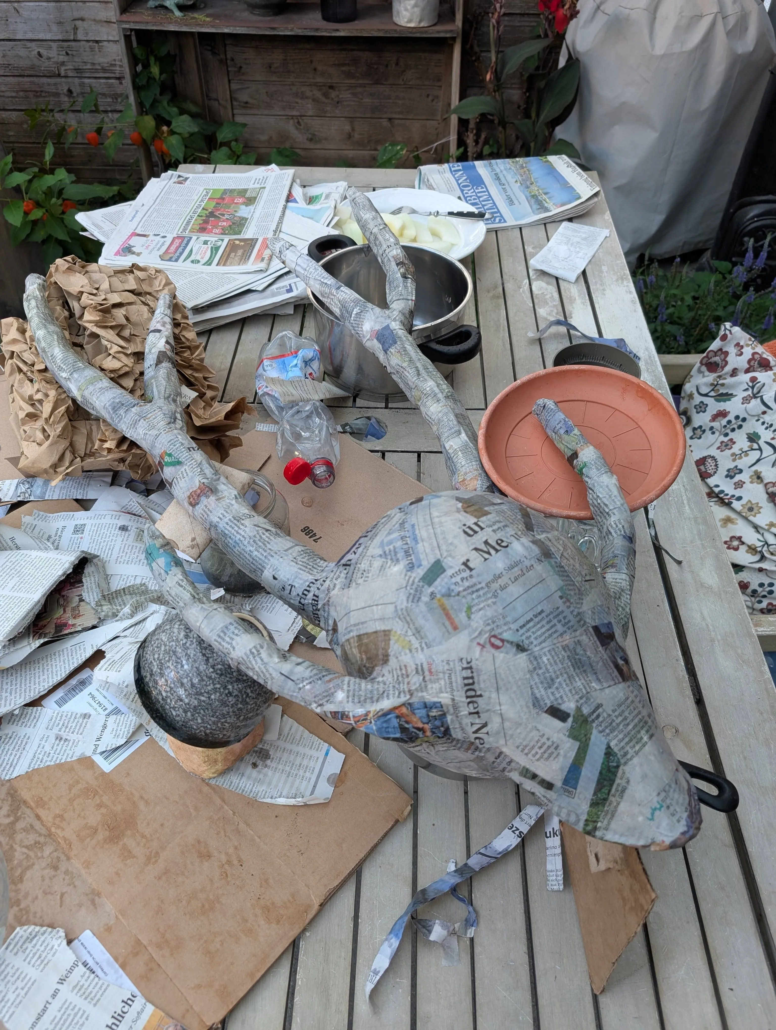 The mask made of paper mache laying on the table outside, with horns that are way too tall.