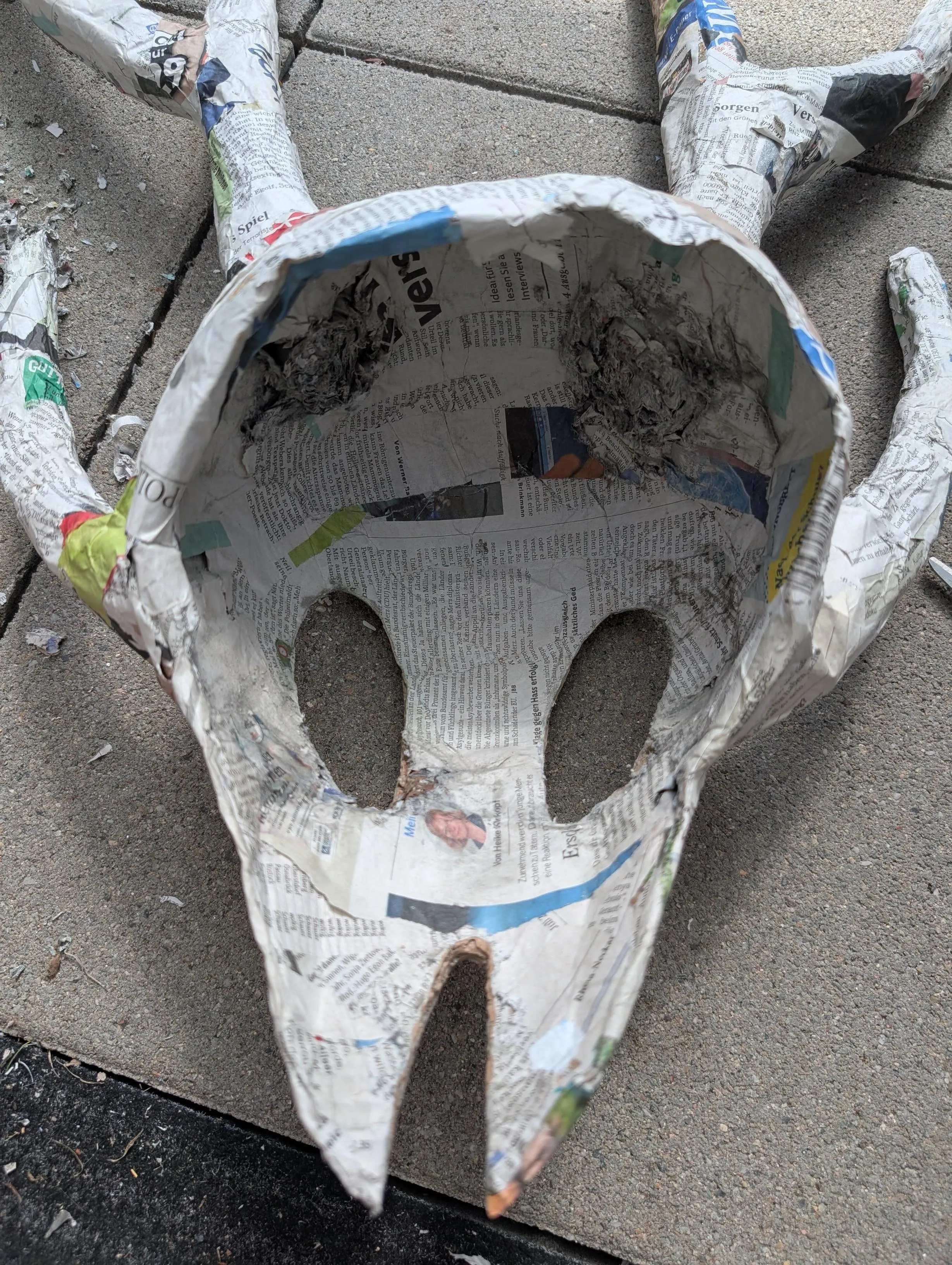 The mask made of paper mache laying on the ground outside, with the eye holes cut out.