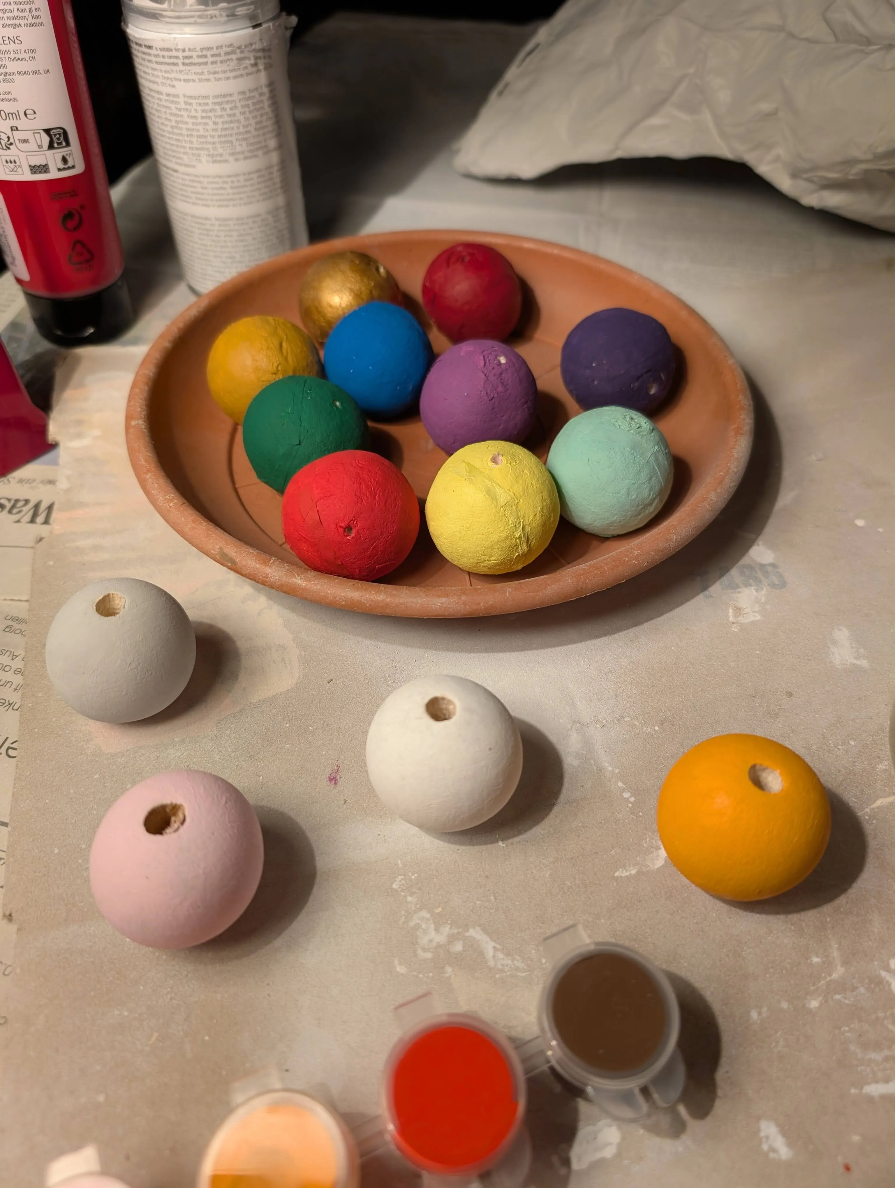 A variety of pearls made of cotton spheres and wood painted in various colors, holes are drilled through their centers to be strung up.
