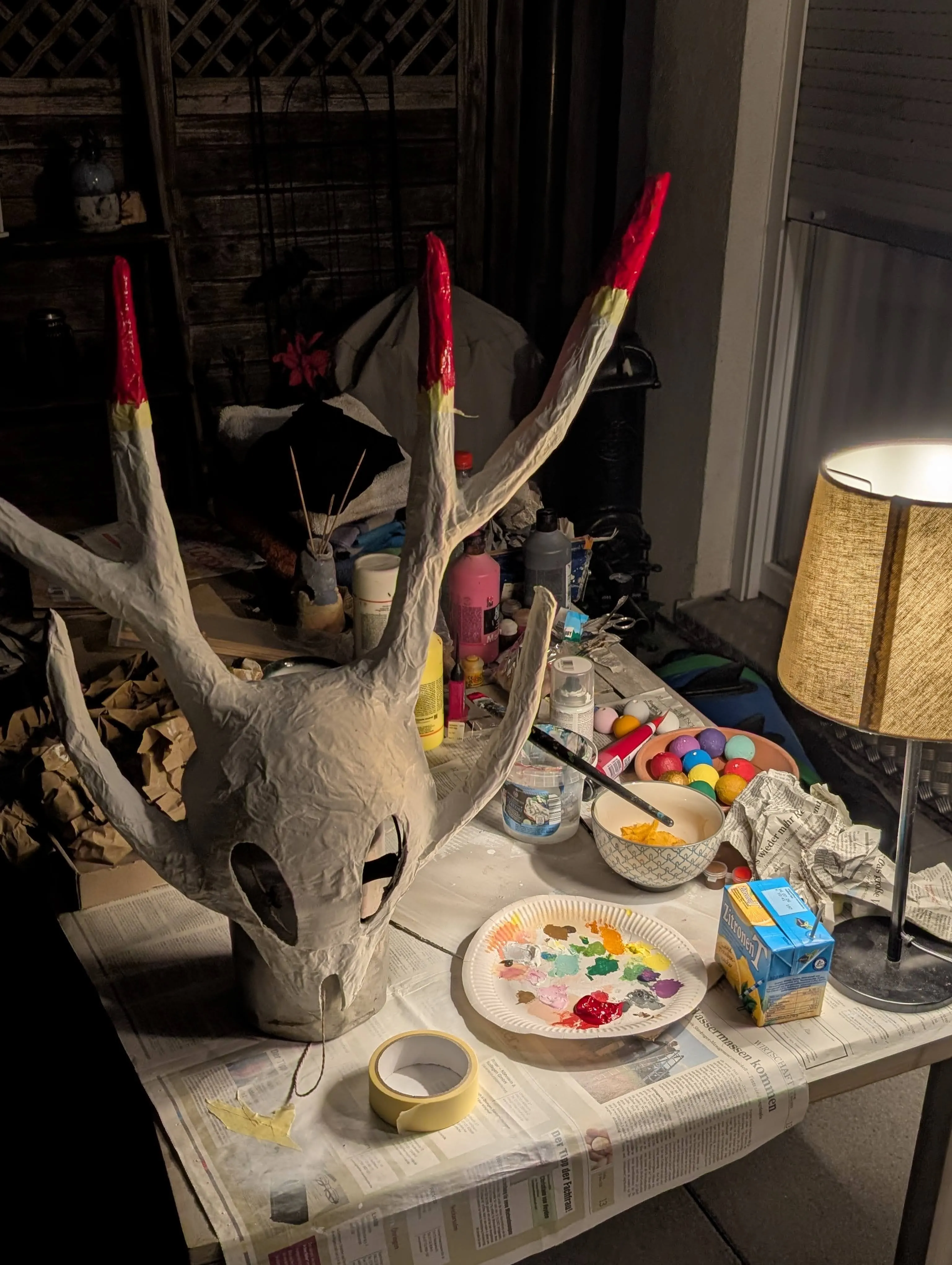 The mask standing on a pot on a messy table being painted in red.